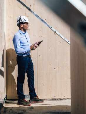 Graf‑Holztechnik Mitarbeiter hält Tablet und betrachtet das Bauvorhaben