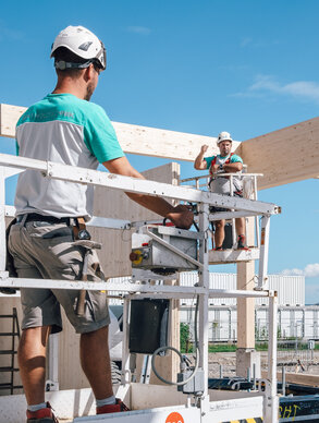 Ein Graf‑Holztechnik Mitarbeiter steht auf einem Steiger im Hintergrund ist eine Baustelle zu sehen
